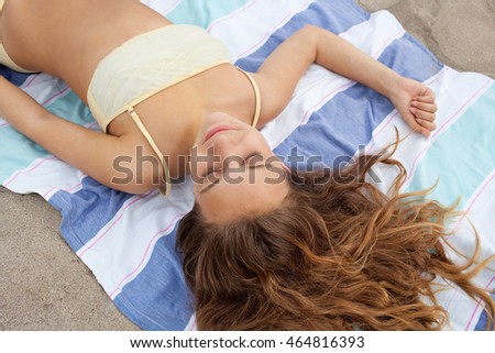 Over head portrait of beautiful young adolescent woman laying down on a beach towel on the sand, sunbathing and relaxing on a summer holiday, nature exterior. Travel lifestyle outdoors.
