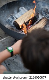 Over The Head View Of A Boy Grilling Hot Dog On A Stick Above An Open Fire In A Cast Iron Grill In Domestic Backyard.