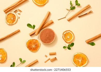 Over a minimalist background, cinnamon (Cinnamomum) sticks, dried orange slices and a dish of cinnamon powder with some green leaves are displayed. These herbals help enhance people’s health