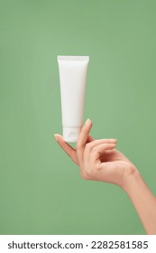 Over a pastel green background, woman hand model holding a white tube without label. Beauty product mockup. Natural skincare products concept - Shutterstock ID 2282581585