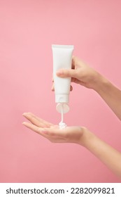 Over a pink background, a hand model squeezing cream from a white unlabeled tube. Cosmetic product advertising