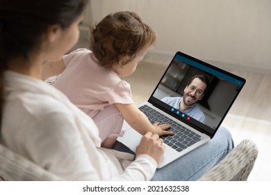 Over shoulder close up view of young Caucasian mom with toddler baby daughter speak talk on video call on laptop with smiling father. Mother with newborn kid have online communication on computer. - Powered by Shutterstock