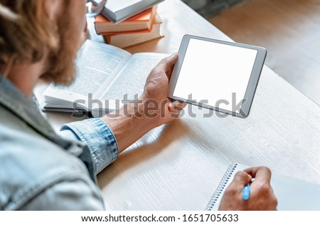 Over shoulder close up view young man student using modern app hold digital tablet pad pc tab make notes write in notebook study online empty mock up screen, distance education, e learning concept