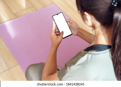 Over Shoulder Closeup View Of Fit Sporty Woman Sit On Mat Holding Phone Mock Up White Blank Screen Video Calling, Watching Online Workout Training Tv Class Video, Using Fitness App At Home In Gym.