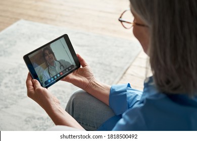 Over shoulder closeup view of old woman patient video calling virtual doctor using tablet at home. Online telemedicine chat meeting. Seniors ehealth, telehealth consultation, tele medicine concept.