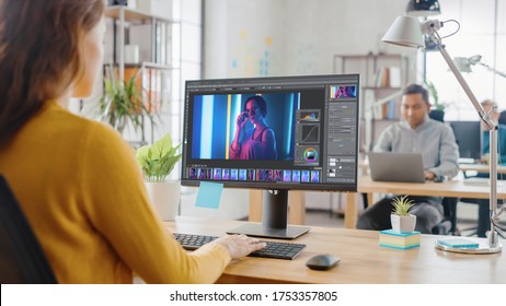 Over The Shoulder: Creative Young Woman Digital Editor Works In Photo Editing Software On Her Personal Computer With Big Display. In The Background Loft Office With Diverse Team Of Young Professionals