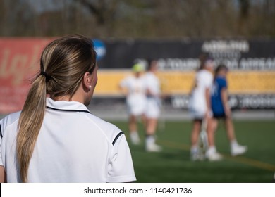 Over The Shoulder Female Head Coach On Sidelines Yelling Play Call To Girl Soccer Players On Field Competing Tournament Match Game On Bright Summer Day In Outside Stadium