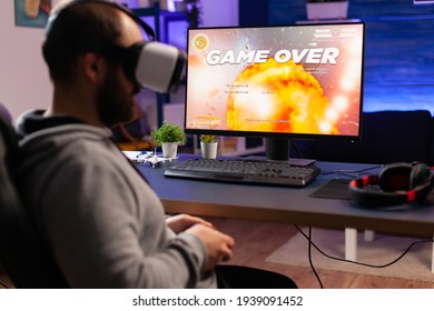 Over Shoulder Of Focused Cyber Player Wearing Virtual Reality Headset During Online Championship. Game Over For Pro Gamer Using Console For Shooter Gaming Competition Late At Night In Living Room