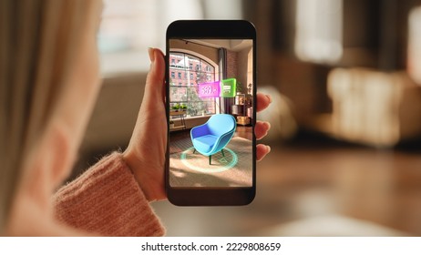 Over the Shoulder Footage of a Female Hand, Holding Smartphone with an Augmented Reality Display Showing a Chair. Woman Doing Online Shopping and Checking her Options In Live Situation In Distance - Powered by Shutterstock