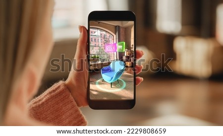 Over the Shoulder Footage of a Female Hand, Holding Smartphone with an Augmented Reality Display Showing a Chair. Woman Doing Online Shopping and Checking her Options In Live Situation In Distance