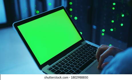 Over the shoulder IT male administrator keyboarding on laptop chrome key green screen, running server diagnostics in database cabinet. Close-up worker with mock-up notebook at data center. - Powered by Shutterstock - Get 15% off with code: PIKWIZARD15