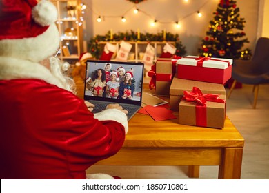 Over shoulder Santa Claus or Father Christmas at laptop computer in his workshop having video call with happy diverse children holding presents. Self-isolation, virtual celebration at home concept - Powered by Shutterstock