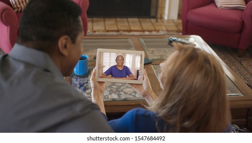 Over The Shoulder Shot Of African American And Caucasian Senior Couple Video Chatting With Sister. Older Friends Facetiming On Tablet Computer