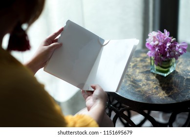 Over The Shoulder Shot Of Asian Woman Adult Is Reading A Pamphlet, Leaflet, Brochure Or Menu. Elegance Home Or Restaurant Setting Concept. Blank Copy Space. Natural Light.