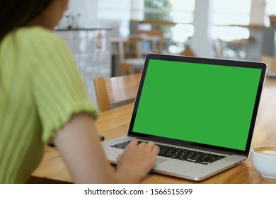 Over The Shoulder Shot Of A Business Woman Working In Office Interior On Pc On Desk, Looking At Green Screen. Office Person Using Laptop Computer With Laptop Green Screen, Sitting At Wooden Table