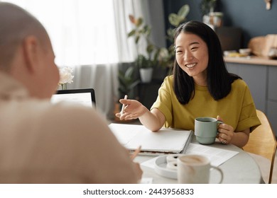 Over shoulder shot of cheerful young Asian woman chatting with her friend while doing homework together - Powered by Shutterstock