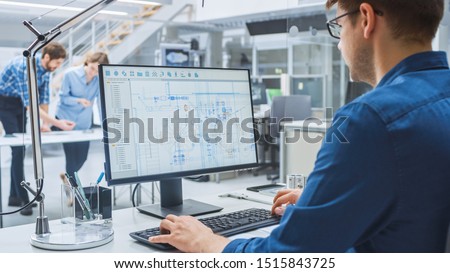 Over the Shoulder Shot of Engineer Working with CAD Software on Desktop Computer, Screen Shows Technical Drafts and Drawings. In the Background Engineering Facility Specialising on Industrial Design