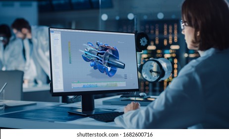 Over the Shoulder Shot: Female IT Scientist Uses Computer Showing CAD Software with Airplane Engine. In the Background Technology Development Laboratory with Scientists, Engineers Working