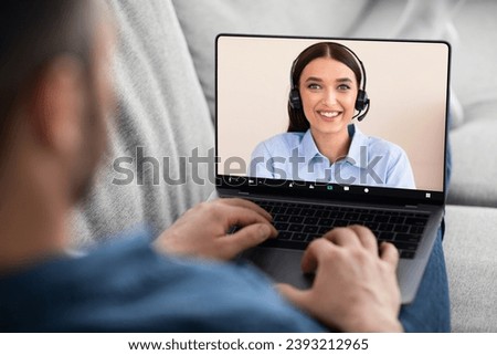 Over shoulder shot of man resting on couch in living room, using newest laptop with video call screen, have video chat with cheerful young woman tech support or financial advisor