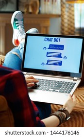 Over shoulder shot of modern hipster in red checkered shirt, jeans and sneakers sitting on sofa in the modern living room getting help from chat robot.
