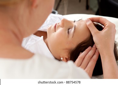 Over the shoulder shot of professional acupuncturist placing needle in face of patient