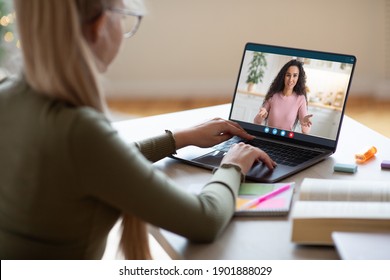 Over shoulder shot of school girl in glasses looking at laptop screen at home, having video call with teacher or tutor, e-education, online studying during pandemic COVID-19 from home