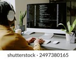 Over shoulder shot of unrecognizable young African American programmer wearing headphones coding on modern desktop computer in office