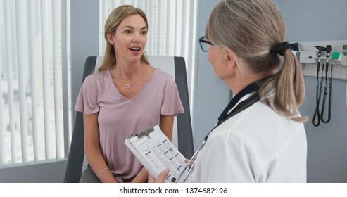 Over the shoulder shot of woman talking to her primary care doctor in exam room. Middle-aged patient having appointment with female senior physician