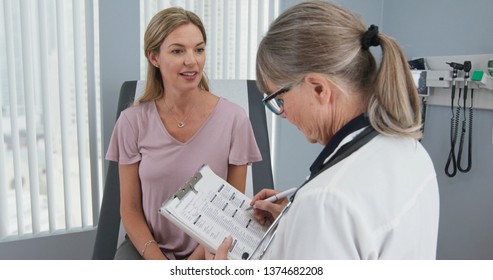 Over the shoulder shot of woman talking to her primary care doctor in exam room. Middle-aged patient having appointment with female senior physician