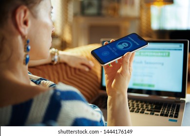 Over Shoulder Shot Of Young Woman Laying On Sofa At Modern Home In Sunnny Hot Summer Day Getting Help From Voice Robot Support While Order Food Digital At Online Supermarket.
