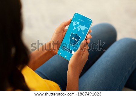 Over The Shoulder View Of African American Woman Using Her Mobile Phone With VPN Virtual Private Network Connection For Secure Traffic, Cyber Security And Personal Data Protection Online