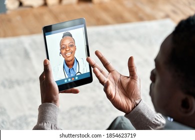 Over shoulder view of african man video calling female virtual doctor consulting patient on tablet at home. Online telemedicine chat visit meeting. Ehealth, telehealth consultation, tele medicine.