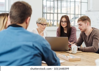 Over the shoulder view of a business meeting with three young people gathered around a laptop computer