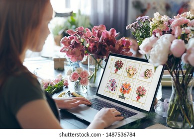 Over Shoulder View Of Busy Flower Shop Owner Standing At Counter With Flowers In Vases And Using Laptop While Choosing Flowers On Internet