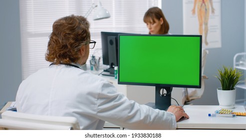 Over shoulder view of Caucasian male physician sitting in hospital cabinet and looking at green screen on computer writing in notebook. Medical consultation, video call with doctor, chroma key - Powered by Shutterstock