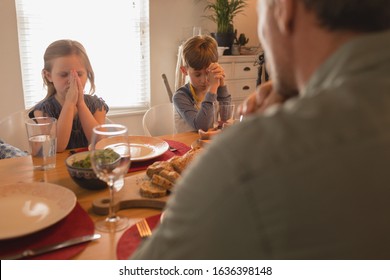 Over Shoulder View Of Family Praying Before Having Food On Dining Table At Home. Social Distancing And Self Isolation In Quarantine Lockdown For Coronavirus Covid19
