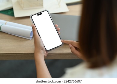 Over shoulder view of female office worker using smart phone while sitting at her working desk - Shutterstock ID 2242766607