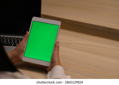 over the shoulder view of hand holding green screen tablet in office