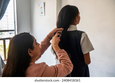 Over the shoulder view of an Indian mother braiding her pre-teen daughters hair as she gets ready for school at their home in Mumbai, India. - Powered by Shutterstock