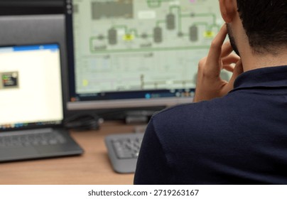 Over the shoulder view of a man analyzing complex process flow diagrams and data on several monitors in a professional office setting
