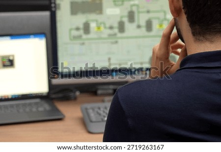 Over the shoulder view of a man analyzing complex process flow diagrams and data on several monitors in a professional office setting