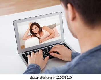 Over the shoulder view of a man having a videochat with his attractive young girlfriend whose picture is shown on the screen