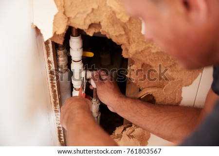 Over shoulder view of middle aged man repairing burst pipe