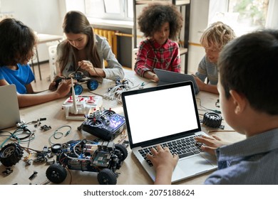 Over shoulder view of multicultural schoolkids building robots developing program for software robotics engineering typing using white empty screen laptop for STEM education advertising. - Powered by Shutterstock