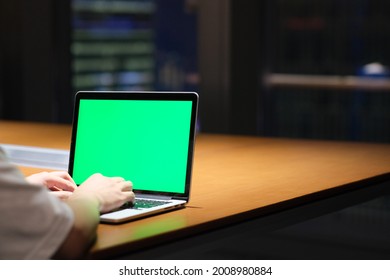 Over The Shoulder View Of People Using Green Screen Laptop Computer On Table In Office At Night