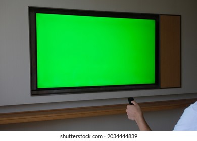 Over The Shoulder View Of People Watching Large Green Screen TV On Wall