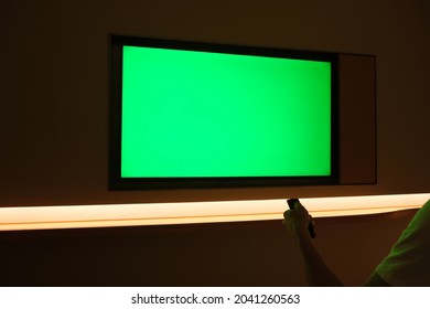 Over The Shoulder View Of People Watching Large Green Screen TV On Wall At Dark Night