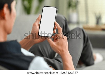 Over shoulder view of relaxed man sitting on couch and using smart phone. People, technology and lifestyle concept