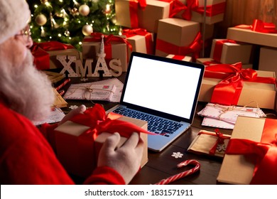 Over shoulder view of Santa Claus holding xmas gift using laptop computer with white blank empty mock up screen monitor for e commerce website ad sitting at decorated table on Merry Christmas eve. - Powered by Shutterstock