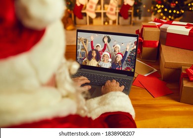 Over shoulder view of Santa Claus or Father Christmas having video call with happy diverse children on laptop computer in his workshop. Self-isolation and virtual online celebration at home concept - Powered by Shutterstock